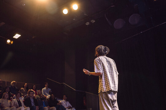Rear view of young male keynote speaker with braided hair explaining in seminar to audience at theater