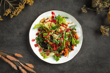 Fresh mixed salad with greens, roasted vegetables, nuts and berry dressing served on a white plate