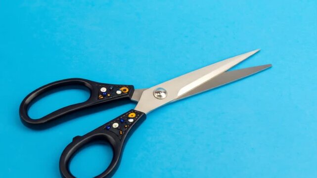 A pair of scissors, black handles with decoration, lay on a bright blue background