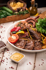 Assorted grilled meats with vegetables, herbs and fried potatoes served on a large round plate