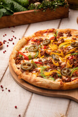 Mexican style pizza with jalapeno slices, ground meat, cheese and vegetables on a wooden board