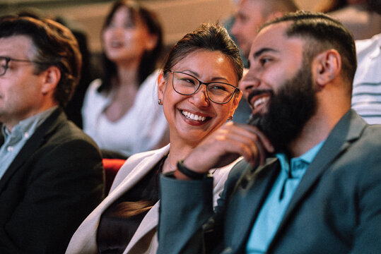 Smiling mature woman talking with male friend while sitting in stage theater