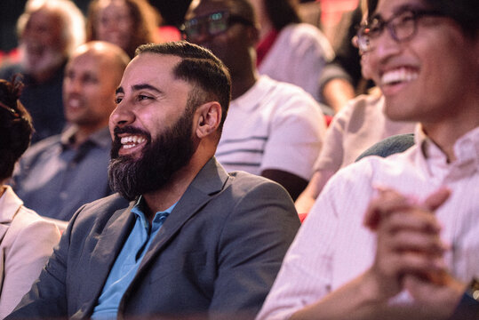 Happy bearded man enjoying stage play while sitting in theater