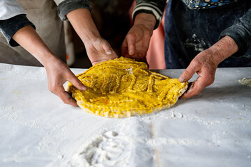 Two elderly women prepare authentic Armenian Gata, shaping dough and nut filling on a floured table, capturing warm homemade culinary tradition.
