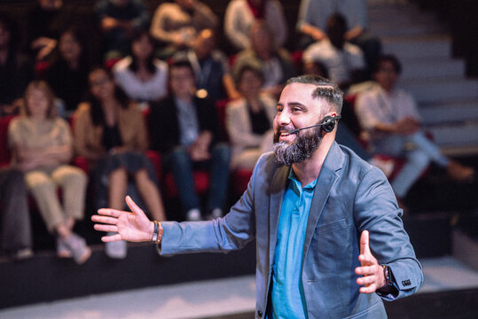 Smiling male presenter wearing headset gesturing while talking in seminar at theater