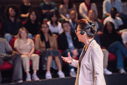 Mature female keynote speaker wearing headset explaining in seminar at theater