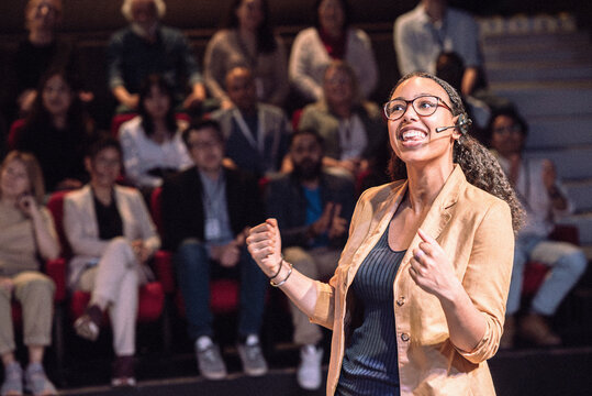 Happy female keynote speaker making fist while talking in lecture at theater