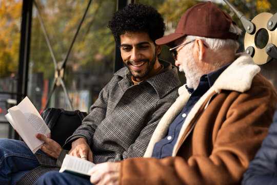 Smiling man spending leisure time with father reading book at bus stop on sunny day