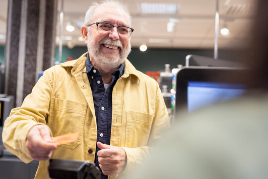 Smiling senior man giving credit card to cashier at supermarket checkout counter