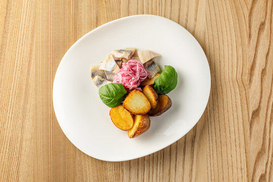 Traditional salted herring served with boiled potatoes and sliced onions, presented as a classic rustic dish.