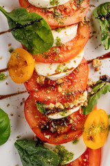 Close-up view of a fresh Caprese salad served on a white plate. Sliced ripe tomatoes layered with creamy mozzarella and garnished with basil leaves. 