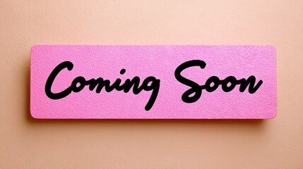 Bright pink sign with bold black lettering stating "Coming Soon," positioned against a soft peach background, creating a vibrant and inviting atmosphere for announcements or promotions