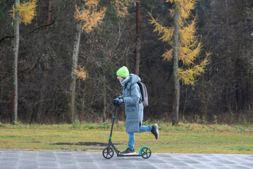 A teenage boy rides a scooter home from school in cold weather.