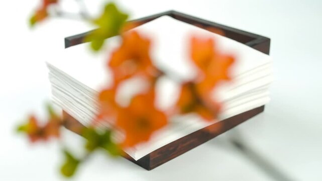 A stack of white papers sit between a floral embellishment of orange flowers and green leaves
