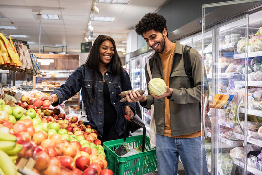 Happy male and female friend choosing vegetables while shopping in grocery store