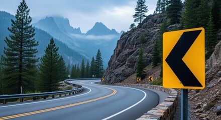 Curved road sign indicating a left turn, surrounded by lush evergreen trees and rocky mountains, creating a scenic view of winding road and natural landscape
