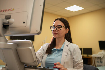 Woman doctor in glasses and lab coat operating an advanced ultrasound machine in a modern clinic,...
