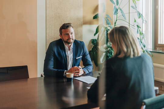 Male business expert listening to female colleague explaining legal agreement while sitting in meeting room at office se