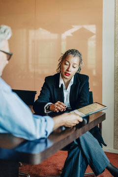 Female lawyer discussing business agreement with colleague on tablet PC while sitting in office board room