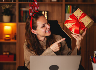 Woman in reindeer antlers showing Christmas gift during holiday video call