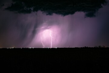 Purple night thunderstorm with lightning above dark horizon
