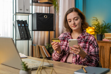 Happy Caucasian woman using bank credit card and smartphone for online shopping payments at home office. Business transaction. Smiling girl freelancer purchases with cellphone E-banking app service.