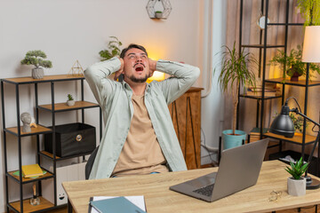 Caucasian young man freelancer shouting, trying not to hear the loud noise from neighbor apartment in building while they renovate home and he cant work on laptop netbook because of the noise.