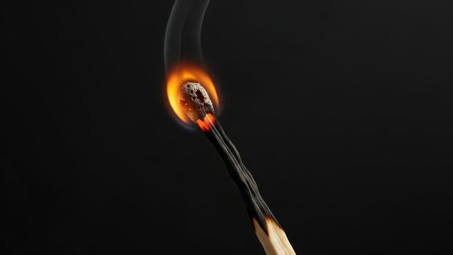 Close up of a burning matchstick with bright orange flame against a dark background