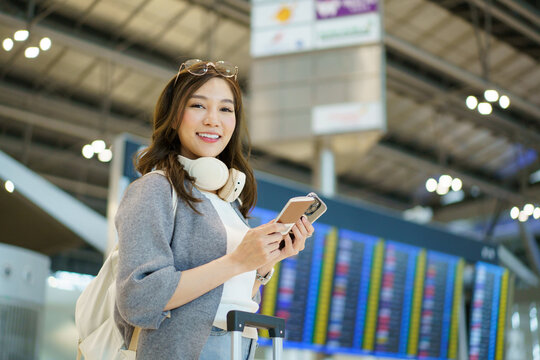 Asian woman checking flight departure board inside an international airport.