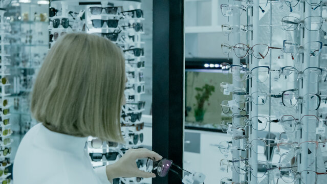 A woman in an optical shop is examining a pair of glasses frames