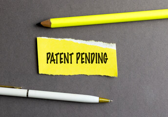 Patent pending message on yellow torn paper with pencil and pen on dark gray background