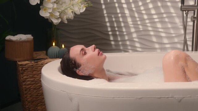 Relaxing gorgeous Caucasian woman emerge from hot warm water enjoying foamy bath at home bathroom female girl bathtub washing head hair bathing spa stress recreation hygiene procedure bodycare routine