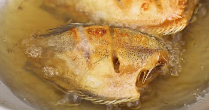 Deep-frying Thai-style snakeskin gourami in hot oil, close-up cooking footage.