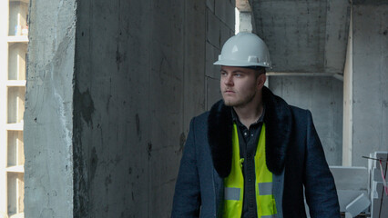 man wearing a hard hat and a high-visibility vest is standing on a construction