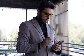 A man is standing on a balcony and looking at his phone