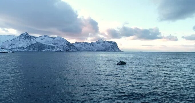 Cinematic aerial drone footage of a small fishing boat on Arctic sea with dramatic snowy mountains and soft pastel sky near Senja in Northern Norway, perfect for travel and adventure content