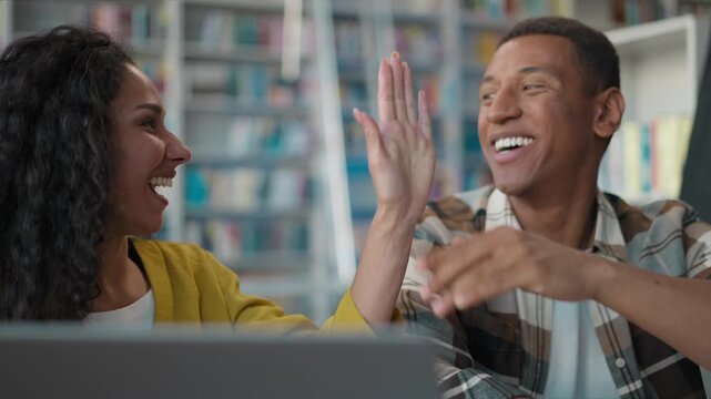 Online success laptop multiethnic couple students giving high five happy African American man Arabian woman using computer device in library project learn task female male study celebrating win result
