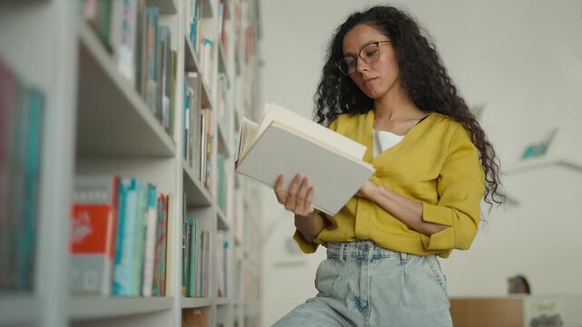 Focused smart active Latina Hispanic woman searching books in library female student girl studying browsing bookcase looking literature textbook find read teacher learner university academic knowledge