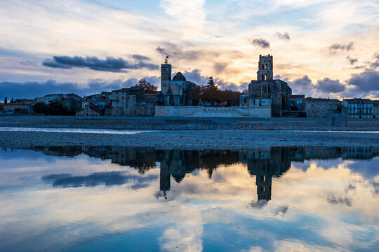 Reflection on the Rhône, from the left bank, of the city of Pont-Saint-Esprit with its churches Saint-Saturnin and Saint-Pierre at sunset