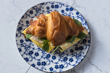 Croissant sandwich with cheese and greens on floral plate in natural light.