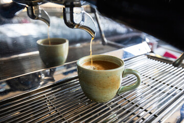 Espresso pouring into ceramic mug from machine in sunlit café with reflections