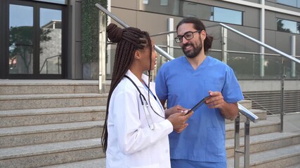 Video of Two diverse doctors discussing medical information on a tablet in front of a hospital - Powered by Adobe