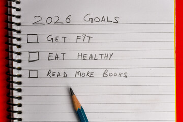 2026 goals list with push pins, an indoor plant and a sticky note on red background. Creative New...