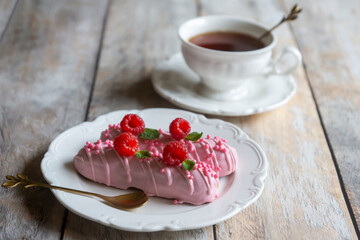 A cup of aromatic, hot tea and raspberry eclairs on a light table.