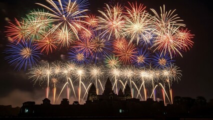 A spectacular display of vibrant, multicolored fireworks exploding in the night sky over a silhouetted city skyline.