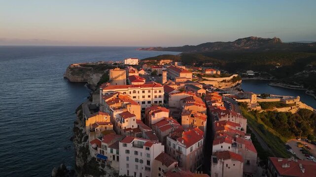 Expansive Aerial Drone Shot Reveals the Historic Bonifacio Citadel City Perched on Dramatic White Limestone Cliffs Above the Mediterranean Sea at Golden Hour Sunrise, Corsica, France.
