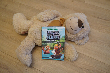 Naklejka premium A plush teddy bear with a Minecraft book on a wooden floor