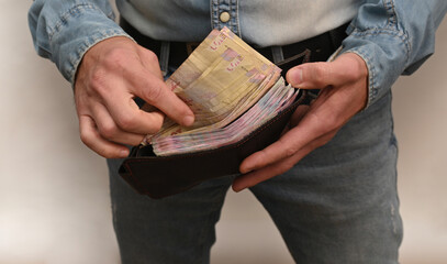 Man holds wallet with visible cash bundle, showing concept of income, earnings, and finance control. Male person checks folded money in wallet, representing wealth and financial awareness.