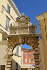 Fototapeta premium Rovinj old town archway showcasing historic architecture and sculpture. Historic stone archway marking an entrance to Rovinj old town street under a clear blue sky.