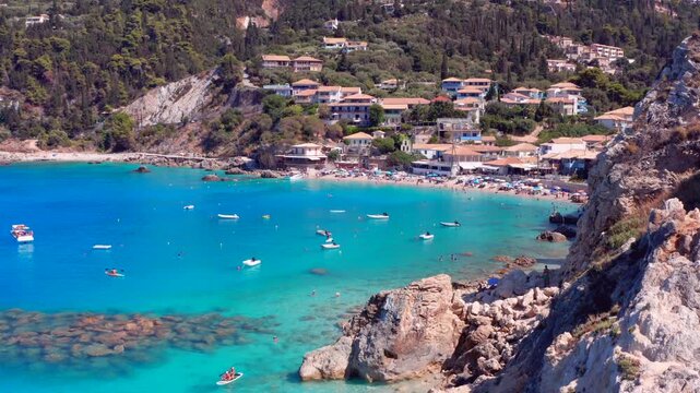 Greece shoreline and typical charming village and blue sea on Greek island. Tourists swimming and small boats in vacation paradise destination Paralia Agios Nikitas